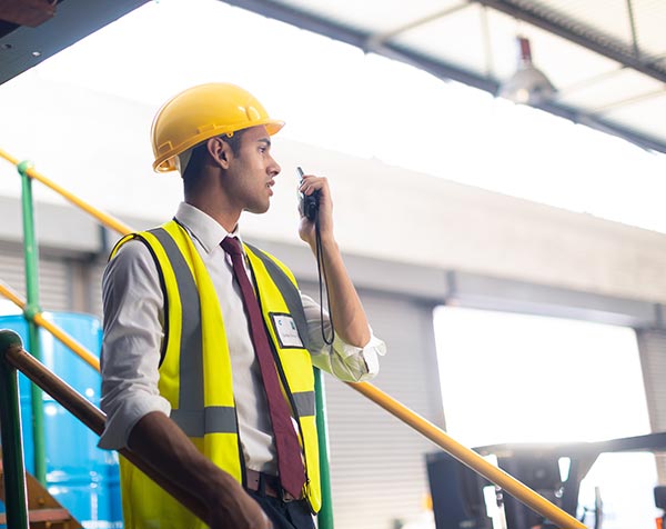 A safety professional in a vest talks on a radio