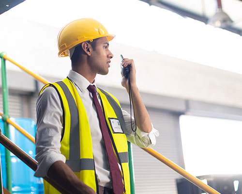 A person in a safety vest and hard hat talks on a hand radio