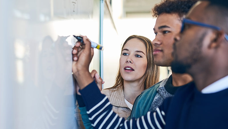 Three students write on a whiteboard