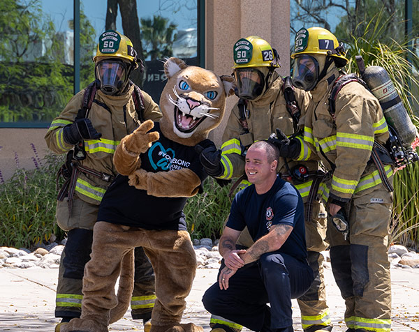 Monty the Mountain Lion poses for photos with firefighters in uniform