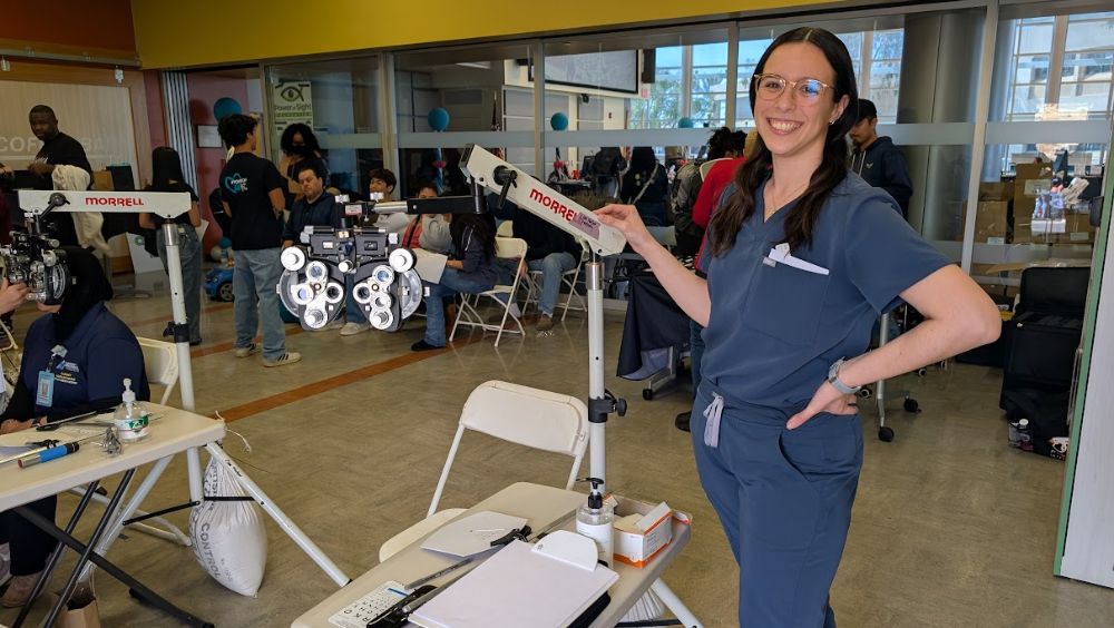 Alumna Christine Castillo Castanon posts next to eye exam equipment
