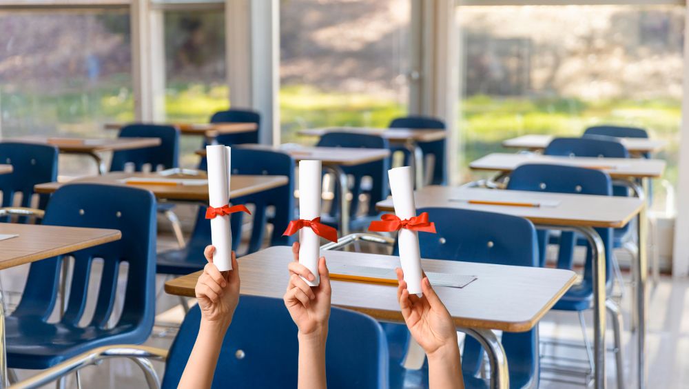 Rolled certificate awards are held up in front of classroom desks, signaling academic success