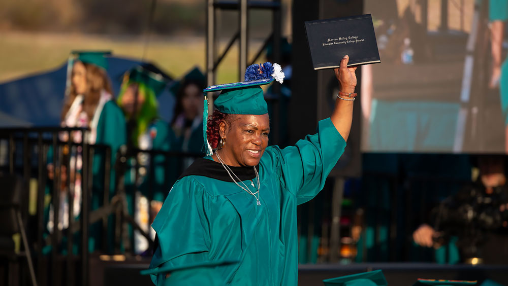 Stacie Jackson, in regalia, walks across the graduation stage.