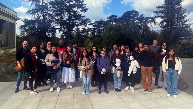 Students stand with professors in a group photo in front of Huntington Library Gardens foliage